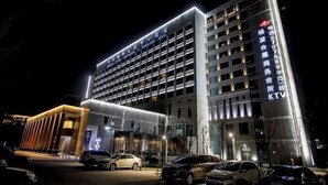 A modern hotel with a multi-story structure, illuminated entrance, and a parking area with several cars. - Yangling International Conference & Exhibition Center Hotel (Xianyang)