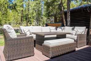 Un conjunto de mobiliario de mimbre para exteriores con cojines, una mesa y un banco, rodeado de árboles y una terraza de madera.