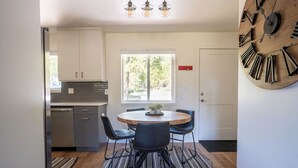 A modern kitchen with a dining area, featuring a round wooden table, black chairs, and a large wall clock. - Peaceful Cabin Nestled in the Pines with a Short Walk to Lake Granby (Granby)