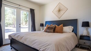 A bedroom with a large bed, two bedside tables with lamps, a wall-mounted artwork, and a view through the door. - Peaceful Cabin Nestled in the Pines with a Short Walk to Lake Granby (Granby)