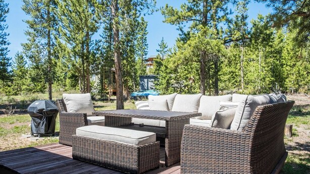 An outdoor wicker furniture set on a wooden deck with a view of a forest and a building in the background. - Peaceful Cabin Nestled in the Pines with a Short Walk to Lake Granby (Granby)