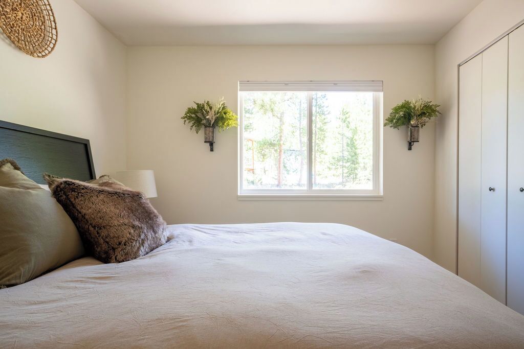 A bedroom with a large bed, a bedside lamp, two wall-mounted planters, and a window with a view of trees.