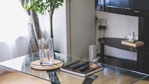 A modern living room with a glass coffee table, a plant, and a television in the background. - Stunning Wembley Flat | 2 Baths (Greater London)