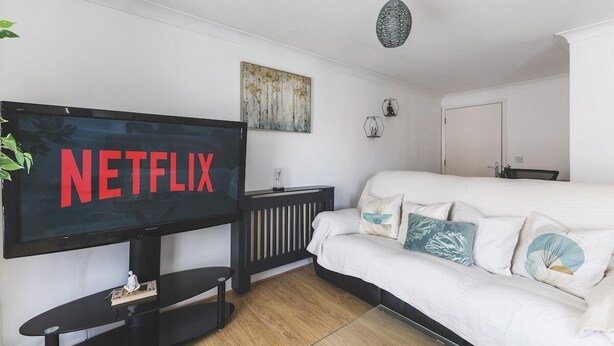 A modern living room with a large flat-screen TV displaying the Netflix logo, a white sofa with decorative pillows, a black entertainment unit, and a wooden floor. - Stunning Wembley Flat | 2 Baths (Greater London)