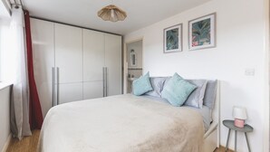 A bedroom with a bed, a wardrobe, a bedside table with a lamp, and two framed pictures on the wall. - Stunning Wembley Flat | 2 Baths (Greater London)