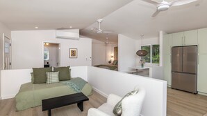 A modern living room with a sofa, a white armchair, a black coffee table, and a ceiling fan.