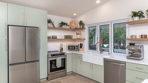 A modern kitchen with stainless steel appliances, light green cabinets, and a window overlooking greenery.