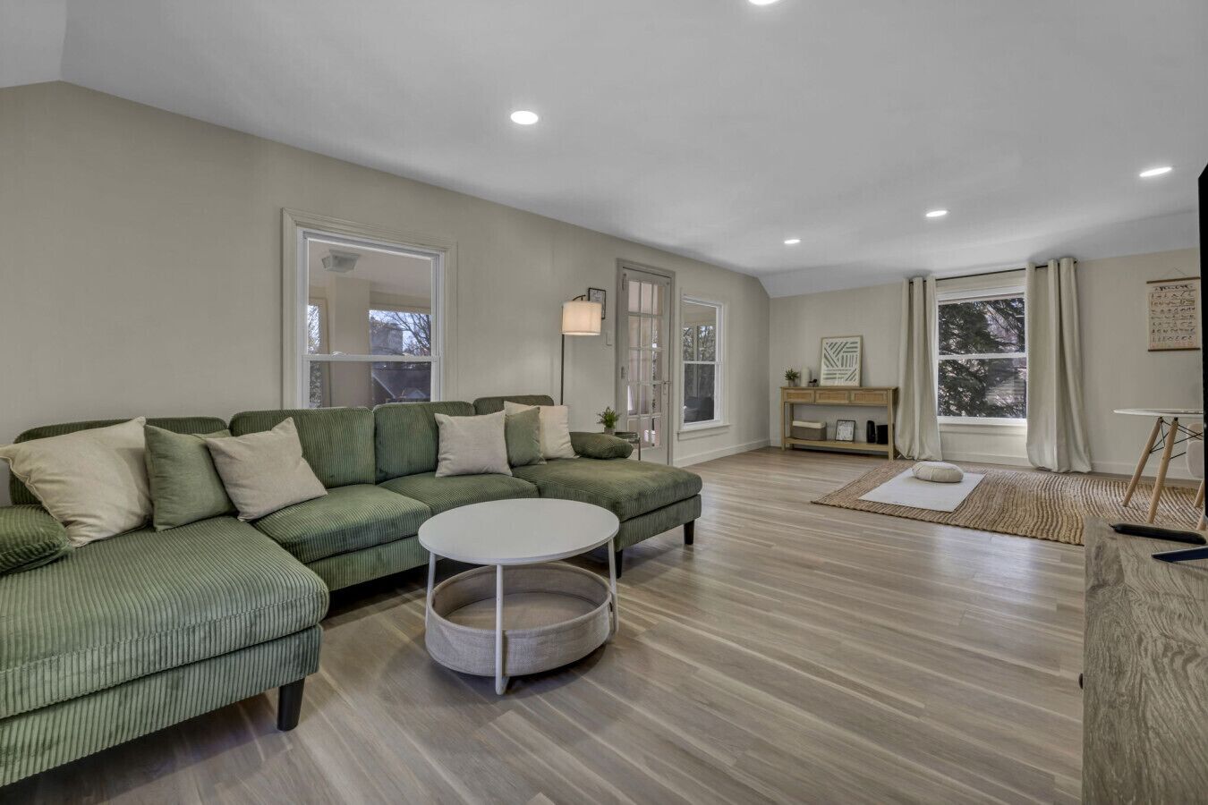 A spacious living room with a green sectional sofa, a round coffee table, and a wooden floor.