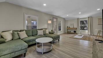 A spacious living room with a green sectional sofa, a round coffee table, and a wooden floor.