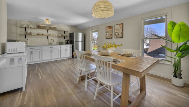 A modern kitchen with white cabinets, a wooden dining table, and a large window. - Escape to comfort at Be Cozy Getaway! Located in a serene neighborhood in Euclid. (Euclid)