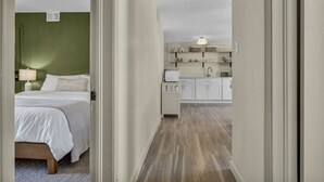 A hotel room with a bed, a nightstand, and a green wall. A hallway leads to a kitchen with white cabinets and a countertop. - Escape to comfort at Be Cozy Getaway! Located in a serene neighborhood in Euclid. (Euclid)