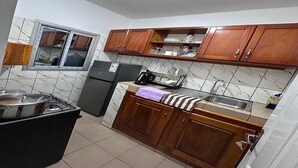A compact kitchen with wooden cabinets, a built-in oven, a refrigerator, and a window above the sink. - Luxury furnished studio (Douala)