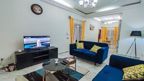 A living room with a television, a blue sofa, a coffee table, and a chandelier. - Luxury furnished studio (Douala)