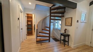 A wooden staircase leading to a second floor, a hallway with wooden flooring, a small table with a vase, and a window with a view of the outside.