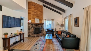 A living room with a stone fireplace, a black leather sofa, a wooden coffee table, and a colorful rug.