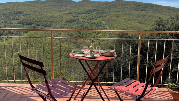 Eine Terrasse mit Tisch für zwei Personen, Stühlen und Blick auf grüne Hügel.
