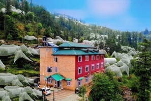 Un immeuble à plusieurs étages, doté d’une façade rouge et d’un toit végétalisé, entouré d’une végétation luxuriante et d’arbres.