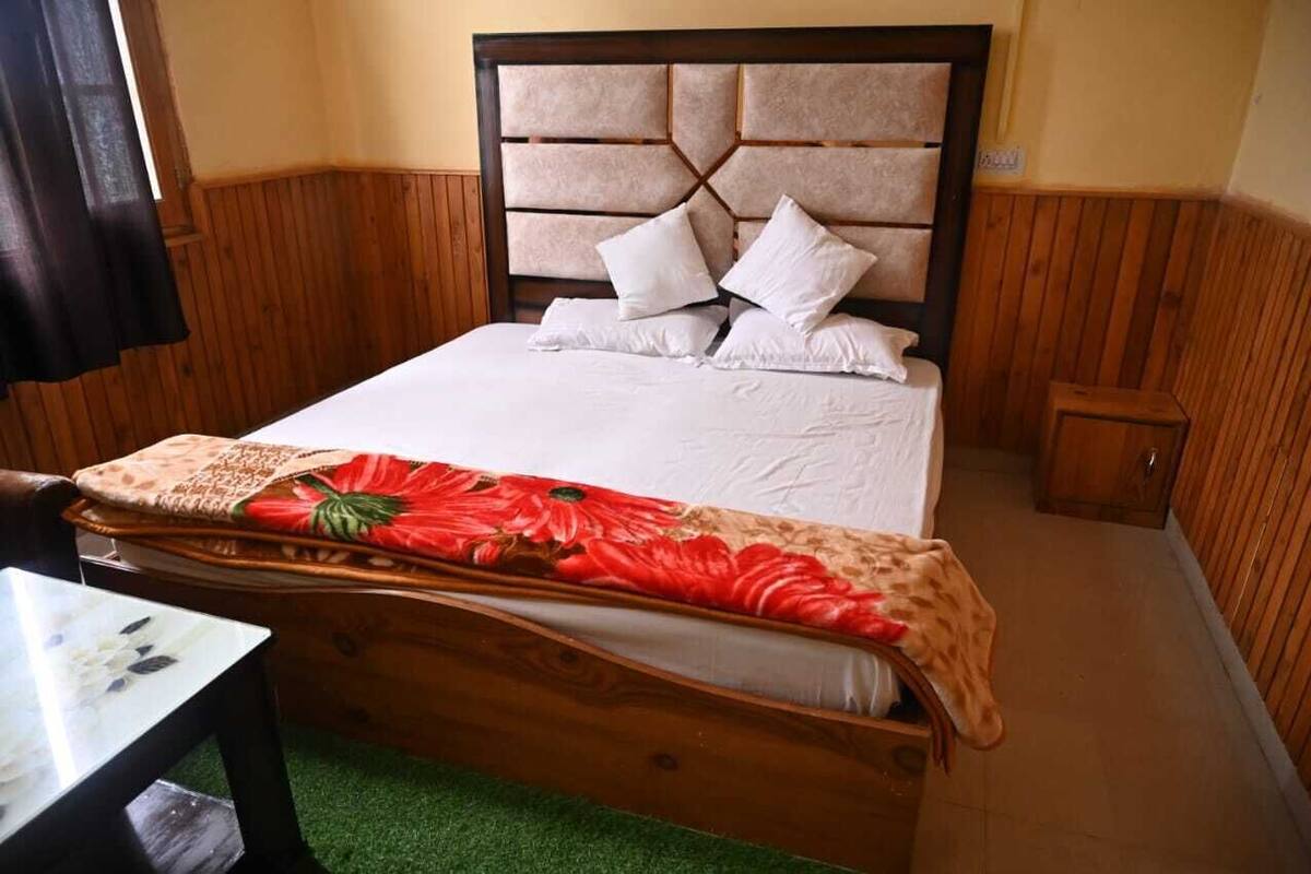 A bed with a wooden headboard, white bedding, and a red floral blanket.