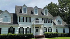 A large, two-story house with a balcony, a front porch, and a well-maintained lawn.