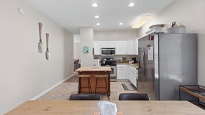 A modern kitchen with white cabinets, a stainless steel refrigerator, and a wooden dining table with a tissue box.