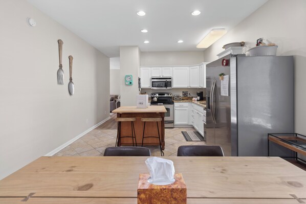 Une cuisine moderne avec des meubles blancs, un réfrigérateur en acier inoxydable et une table à manger en bois, agrémentée d’une boîte à mouchoirs.
