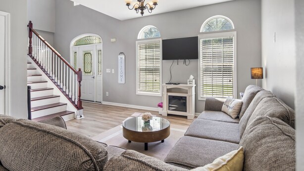 A spacious living room with a staircase, a fireplace, and a large window with blinds.