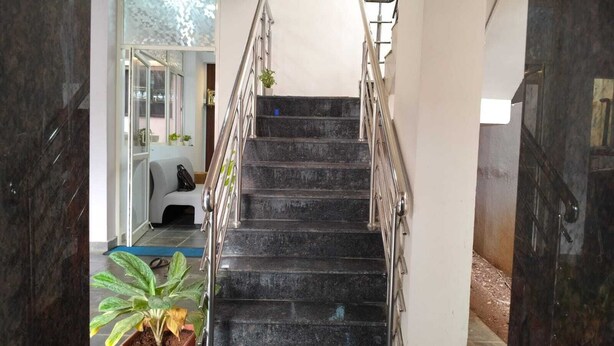 A staircase with metal railings, a potted plant, and a glimpse of a room with a sofa and a window. - Urban Elite Apart Hotel  (Hubli)