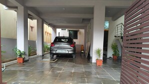 A covered car parking area with a car parked in the middle, potted plants, and a staircase leading to an upper level. - Urban Elite Apart Hotel  (Hubli)