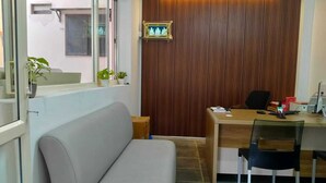 A modern office with a wooden panel wall, a desk with a computer, and a grey sofa. - Urban Elite Apart Hotel  (Hubli)