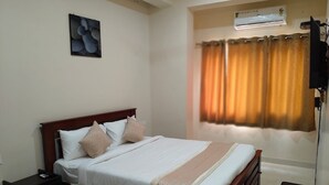 A neatly made bed with a wooden headboard, a bedside table, and a wall-mounted air conditioner. - Urban Elite Apart Hotel  (Hubli)