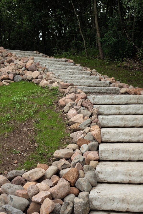 Un sentier pavé de pierres, avec des marches menant à une pente, bordé d’un mélange de gros et de petits rochers.