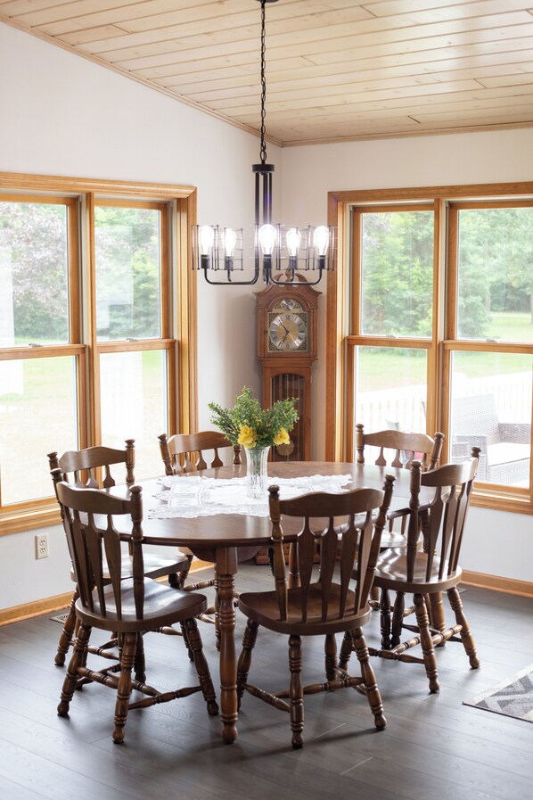 A dining room with a wooden table, six chairs, a vase with flowers, and a large window.