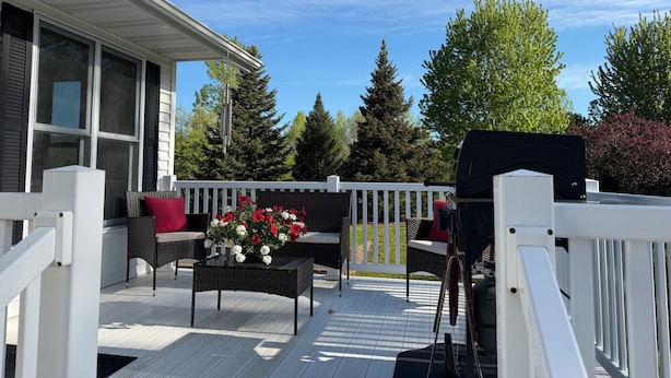 En overdækket terrasse med hvid gelænder, et fletbord med blomsterarrangement og en grill.