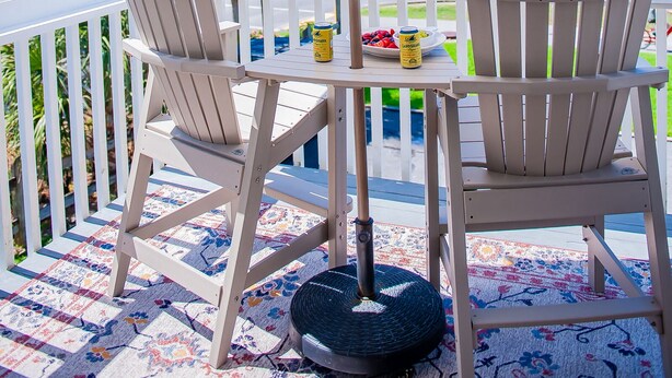 A covered patio with two Adirondack chairs, a table, and a large umbrella. The patio overlooks a beach with palm trees and the ocean. - Family Tides (Destin)