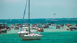 A marina with multiple boats docked, a clear sky, and a distant cityscape. - Family Tides (Destin)
