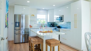A modern kitchen with stainless steel appliances, a marble island, and wicker bar stools. - Family Tides (Destin)