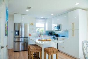 Una cocina moderna con electrodomésticos de acero inoxidable, una isla de mármol y taburetes de mimbre.