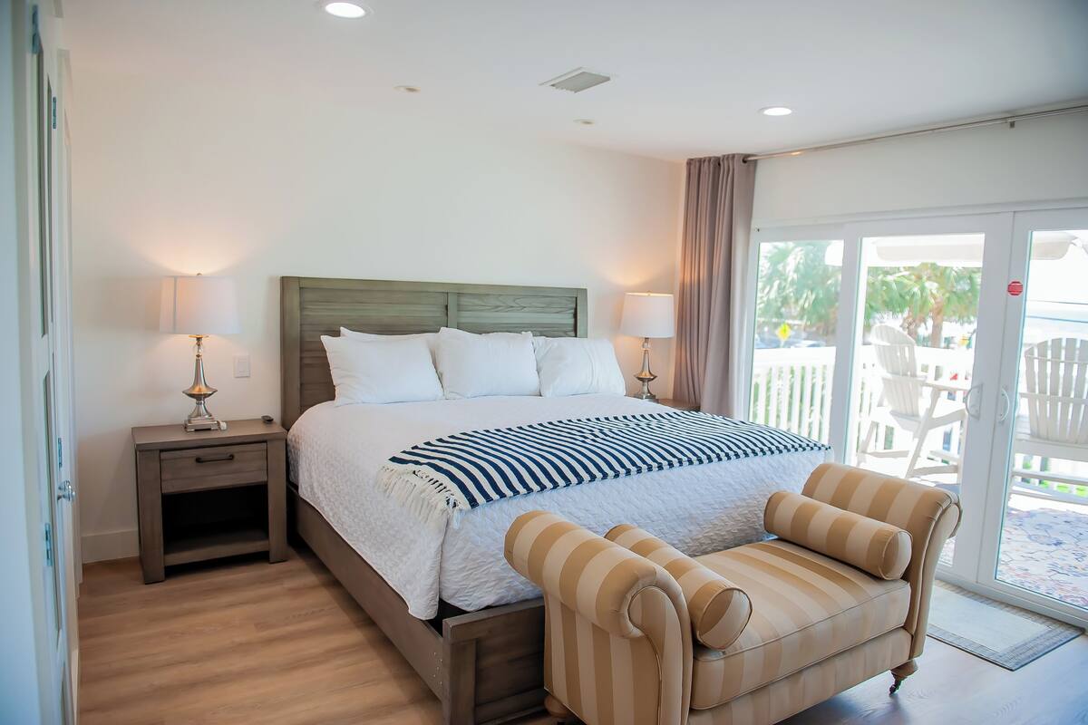 A hotel room with a large bed, two bedside tables, a chair, and a view of the outside through a glass door.