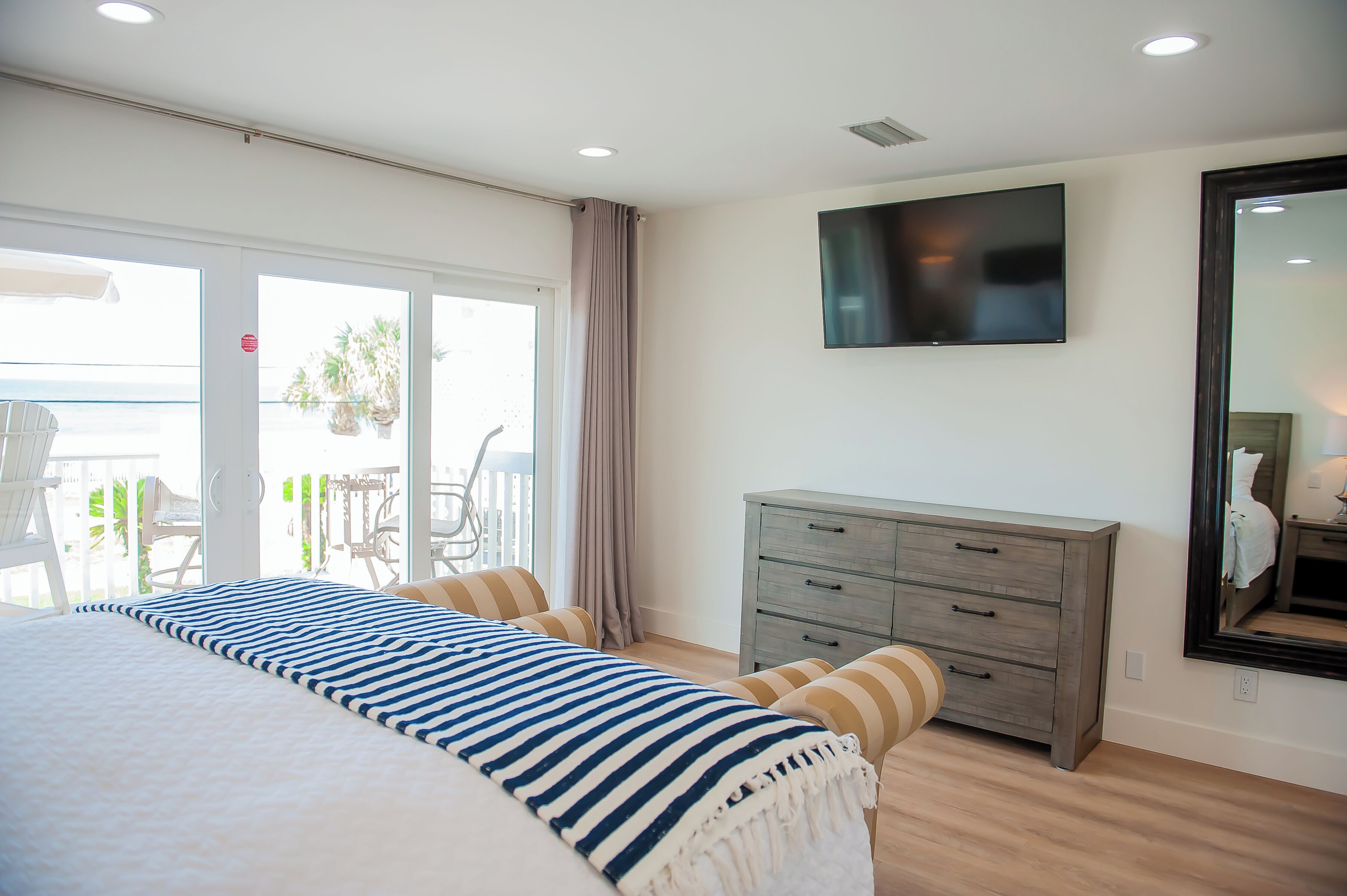 Een slaapkamer met een groot bed, een dressoir, een televisie en een balkon met tuinmeubilair.
