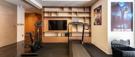 Un gimnasio con cintas de correr, una bicicleta estática y una televisión instalada en la pared.