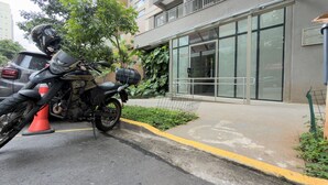 A motorcycle parked in front of a building with a glass facade, a metal railing, and a visible door. - Studio p. Allianz e Hosp Albert Einstein (São Paulo)