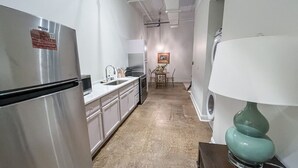 Una cocina estrecha con electrodomésticos de acero inoxidable, un comedor con mesa y sillas, y una lámpara fijada a la pared.