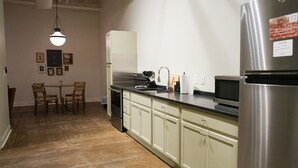 Una cocina con un refrigerador de acero inoxidable, un microondas y un lavabo. Hay una mesa de comedor con sillas y una lámpara colgante.