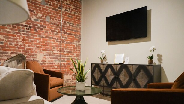Una sala de estar con pared de ladrillo, un televisor de pantalla plana y una mesa de centro de vidrio con una planta.