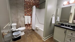 Un baño con pared de ladrillo, inodoro, bañera, lavabo y espejo.
