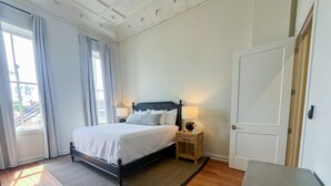 A bedroom with a bed, bedside tables, a door, and a view of the outside. - Cane - The Flats Demopolis (Demopolis)