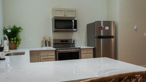 A modern kitchen with a central island, stainless steel appliances, and a dining area with wicker chairs. - Cane - The Flats Demopolis (Demopolis)