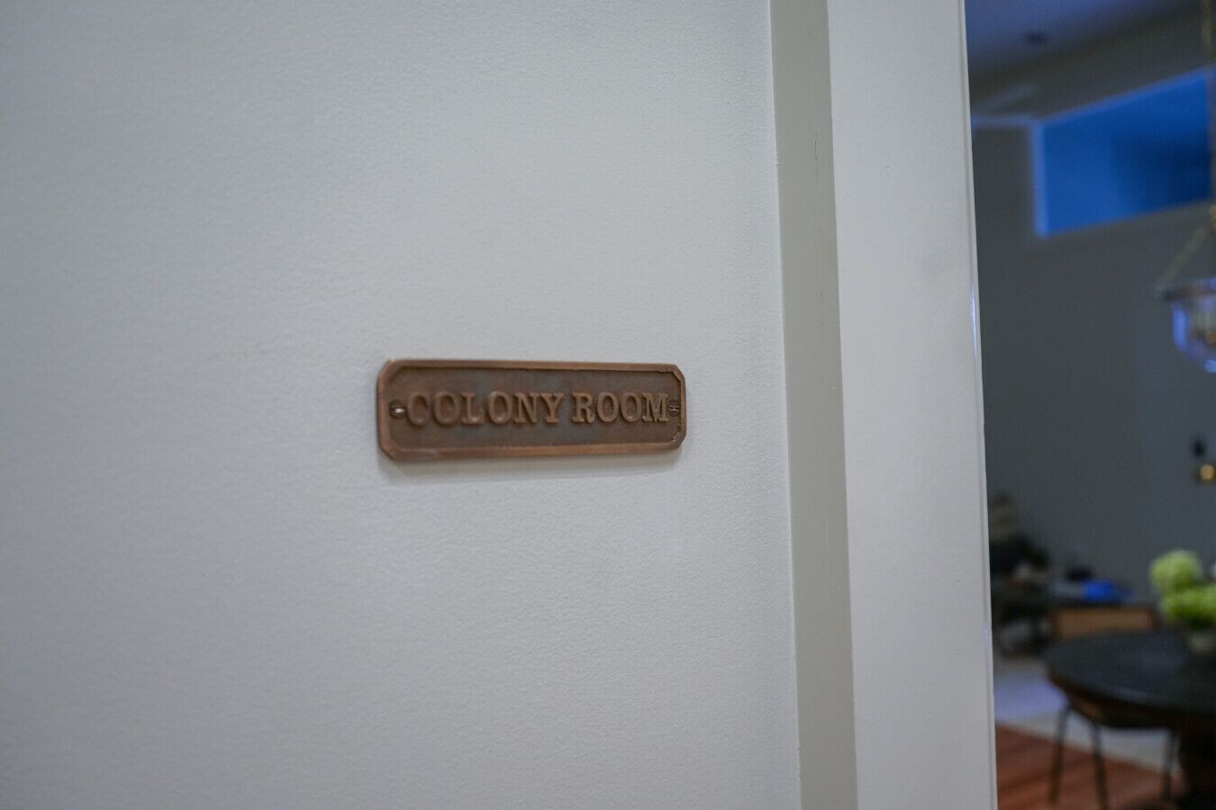 Una señal en una pared blanca que dice 'COLONY ROOM'.