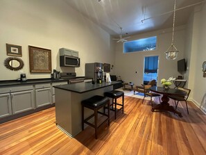 A spacious kitchen with a central island, wooden flooring, and a dining area with a round table and chairs. - Colony -The Flats Demopolis (Demopolis)