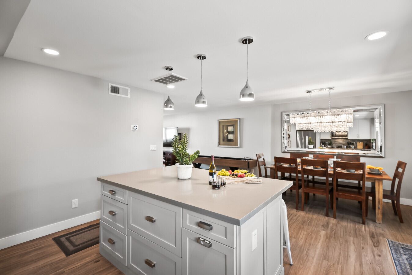 A modern kitchen with a central island, pendant lighting, and a dining area with wooden chairs and a table.